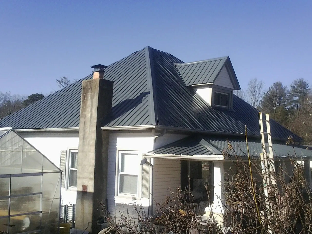 Dark blue standing seam metal roof on a white farmhouse with dormer — Slate & Tile Roof Repair by Roofing Brothers in Lamont