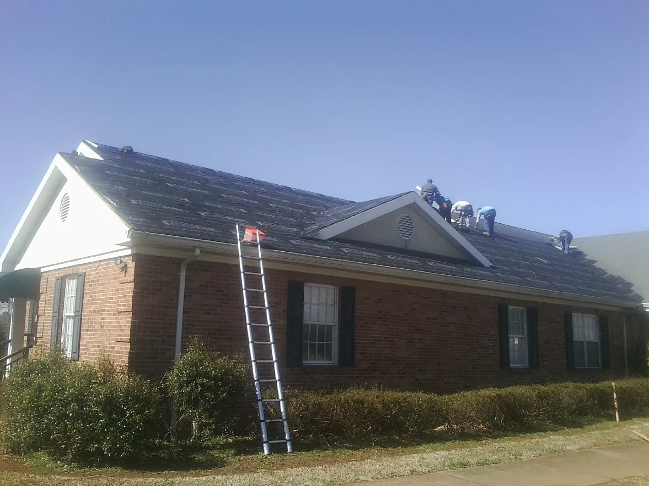 Crew tearing shingles off a brick ranch roof with a ladder set — Emergency Roof Repair work by our crew in Lamont