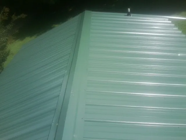 New green metal panels meeting at the ridge of a roof — Flat Roof Repair work by our crew in Lamont