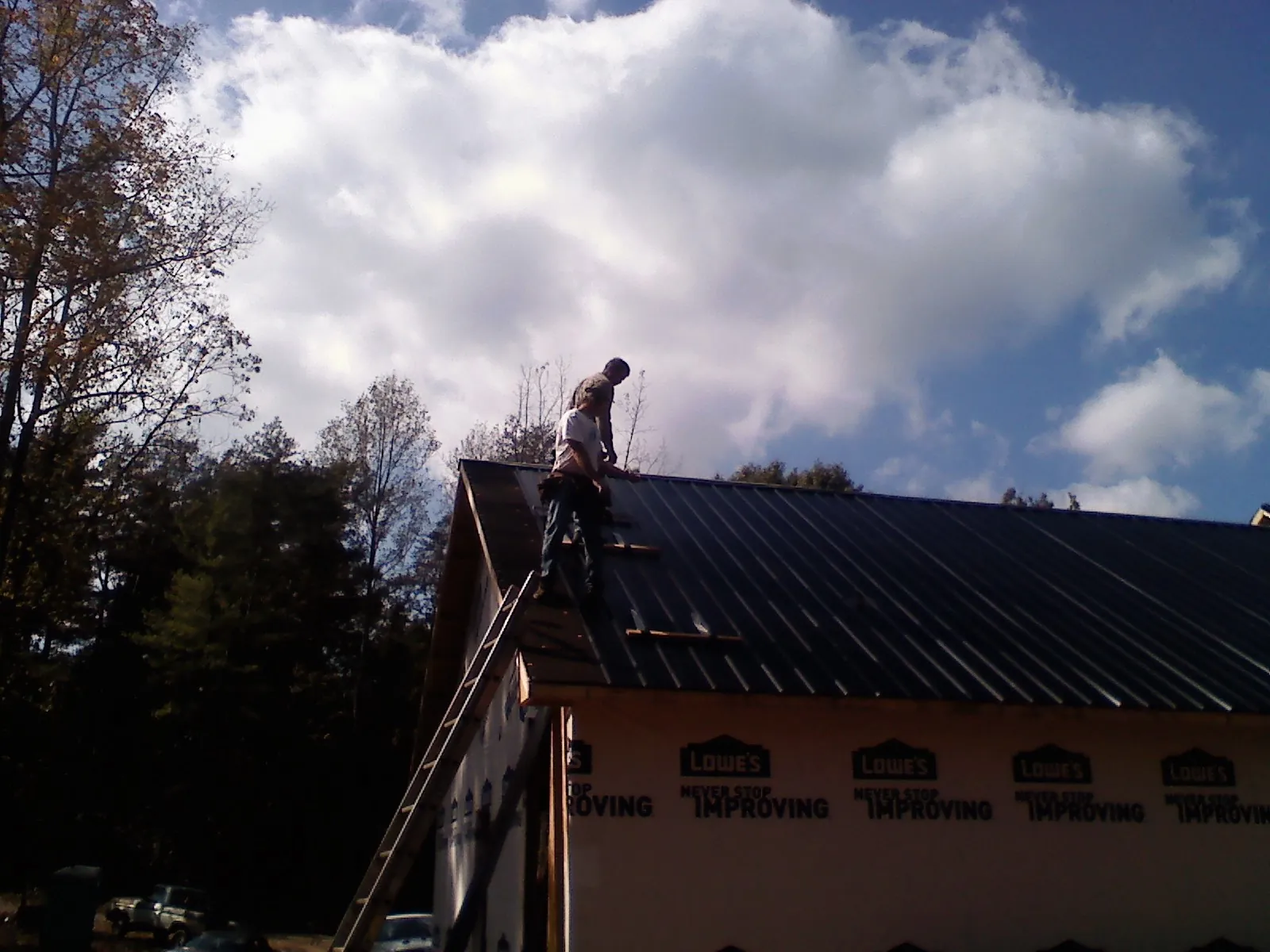 Roofer fastening dark metal panels high against a cloudy sky, from a Roof Inspection job in Lamont